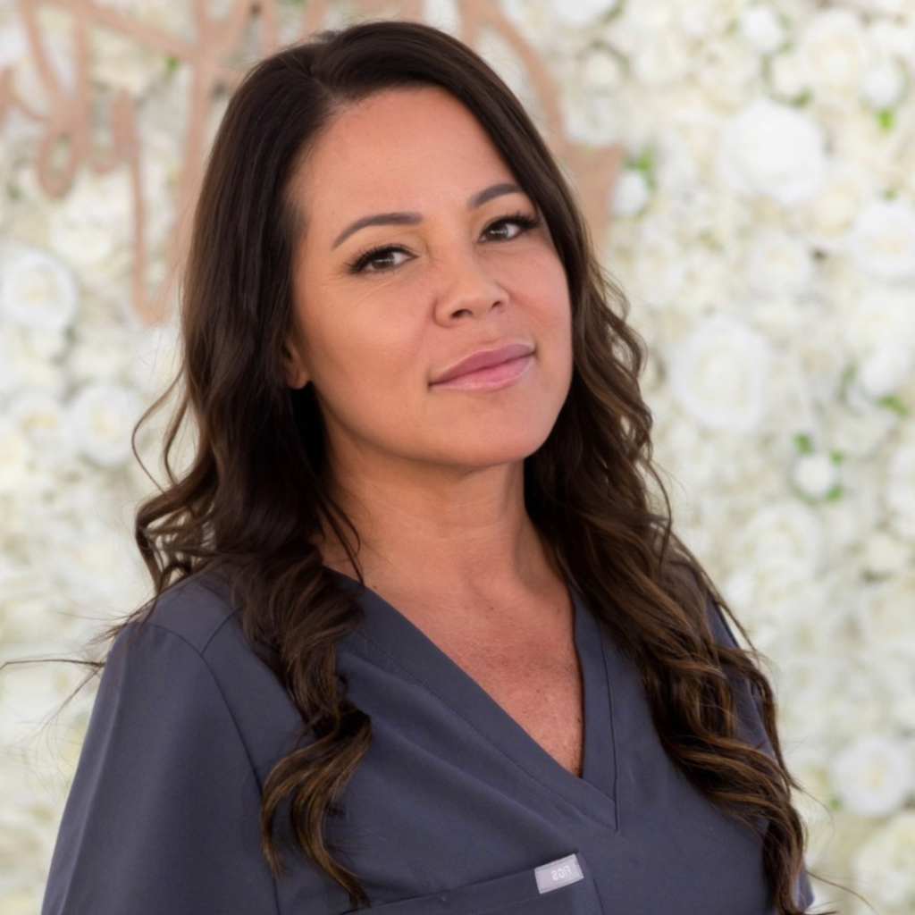 Portrait of Melissa, the founder of Beyond Beautiful, with a warm and confident smile, dressed in professional attire against a backdrop of delicate white flowers.